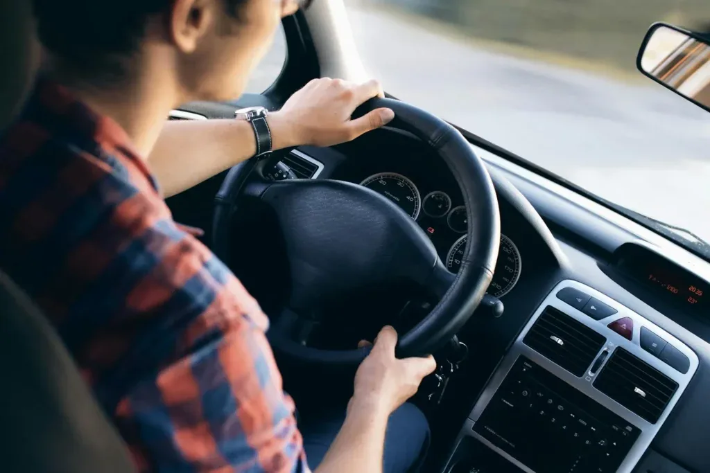 Un homme, portant une chemise à carreux rouge et bleu, en train de conduire une voiture.