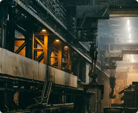 View inside a large, industrial steel mill with dark metal structures and warm lighting