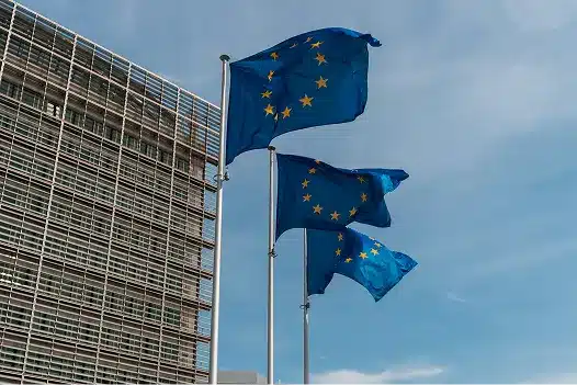 Three European Union flags waving in front of an official building in Brussels.