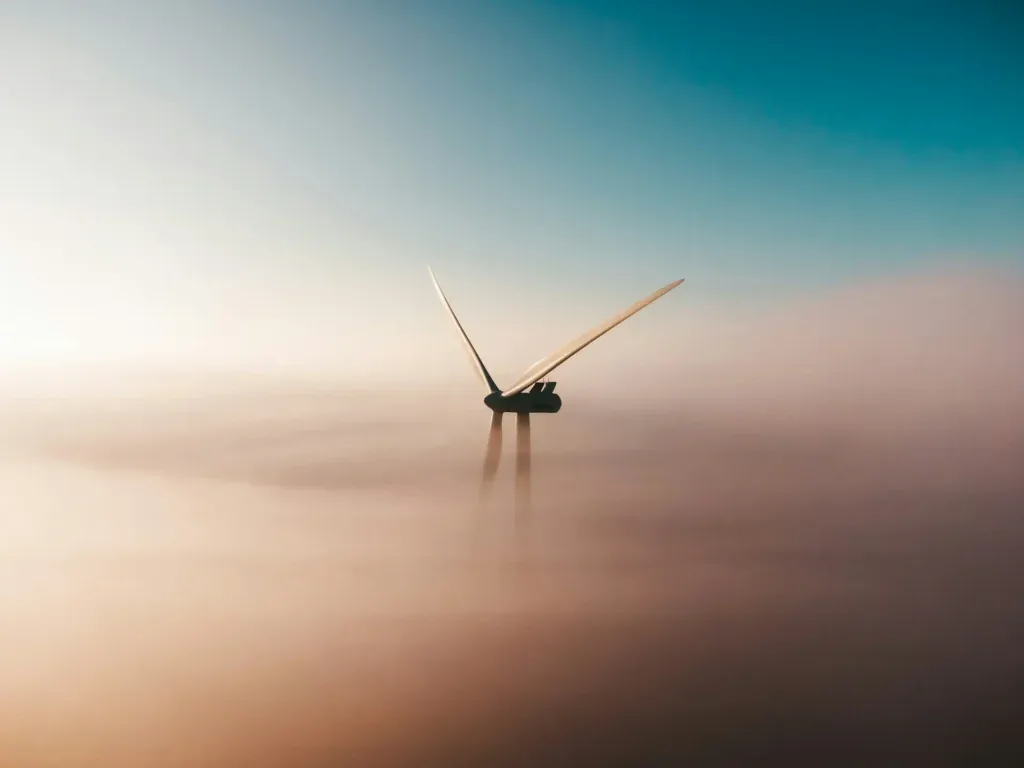 Wind turbine emerging from a sea of fog at dusk